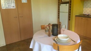 A dining area with a table set for two, a microwave above the cabinets, and a cabinet with a microwave on top.