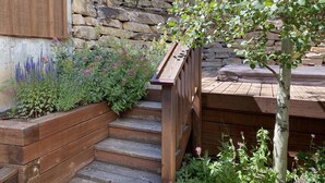 Una escalera de madera que lleva a una terraza con un muro de piedra y diversas plantas.