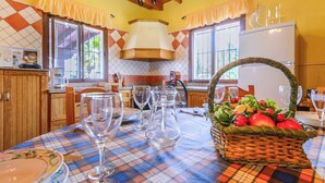 A dining area with a table set for four, a basket of fresh fruit, and a kitchen in the background. - Las Lomas de San Rafael Periana by Ruralidays (Málaga)