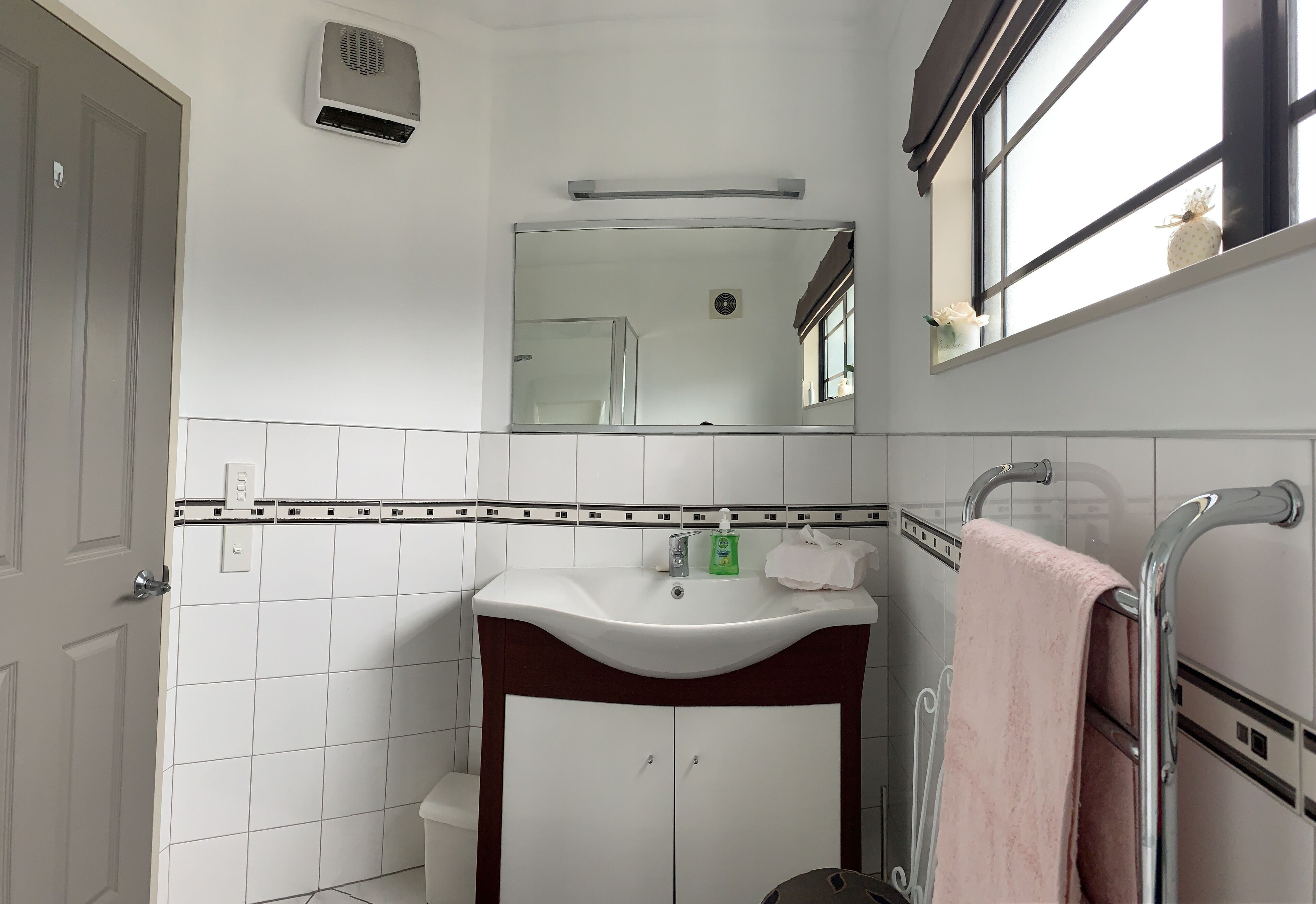 Une salle de bain avec un lavabo blanc, un miroir, un porte-serviettes et une douche.