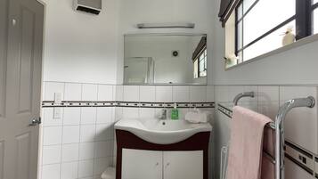 Une salle de bain avec un lavabo blanc, un miroir, un porte-serviettes et une douche.