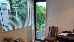 A room with a red sofa, a wooden chair, a small table with a plant and books, and a view through a door to a garden. - Apartment Ahuriri short stroll to beach.<br> (Ahuriri)