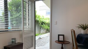 A room with a sliding glass door leading to a garden, a small table with a picture frame, a chair, and a dark wooden cabinet. - Apartment Ahuriri short stroll to beach.<br> (Ahuriri)