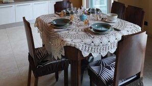 Ein Essbereich mit einem runden Tisch, der mit einer weißen Tischdecke aus Spitze bedeckt ist und von Holzstühlen umgeben wird.