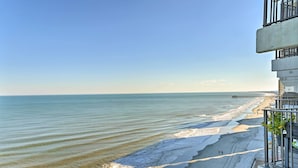 A beach view from a balcony with a clear sky, a sandy beach, and a pier in the distance. - Oceanfront Oasis w/ Deck and Resort Beach Access! (Garden City)
