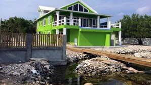 Une maison d’un vert éclatant, dotée d’un balcon blanc, située à côté d’un ruisseau aux rives rocheuses.