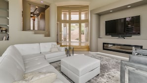 A modern living room with a sectional sofa, a glass coffee table, a flat-screen TV, and a fireplace. - Golfers Paradise in Fountain Hills (Fountain Hills)