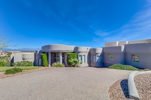 A modern building with a curved facade, a gravel driveway, and landscaped areas with shrubs and a palm tree. - Golfers Paradise in Fountain Hills (Fountain Hills)