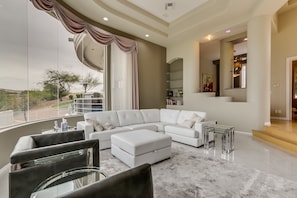 A spacious living room with a large sectional sofa, a glass coffee table, and a view of a landscaped outdoor area. - Golfers Paradise in Fountain Hills (Fountain Hills)