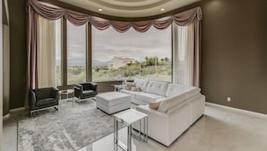 A spacious living room with a large window, a white sofa, a black armchair, and a glass coffee table. - Golfers Paradise in Fountain Hills (Fountain Hills)