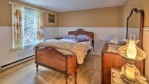 Un dormitorio con cama de madera, mesita de noche, cómoda, espejo y ventana con cortinas.