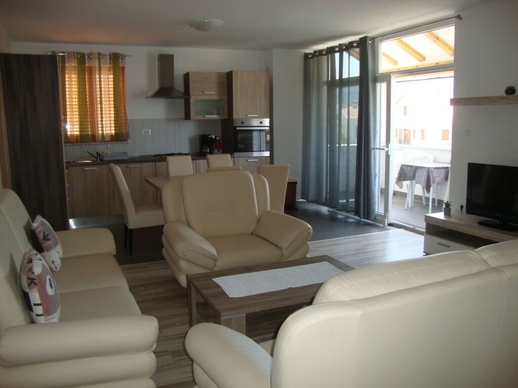Una sala de estar moderna con un sofá, una mesa de centro y un televisor. Cuenta con una zona de cocina con armarios y una estufa.
