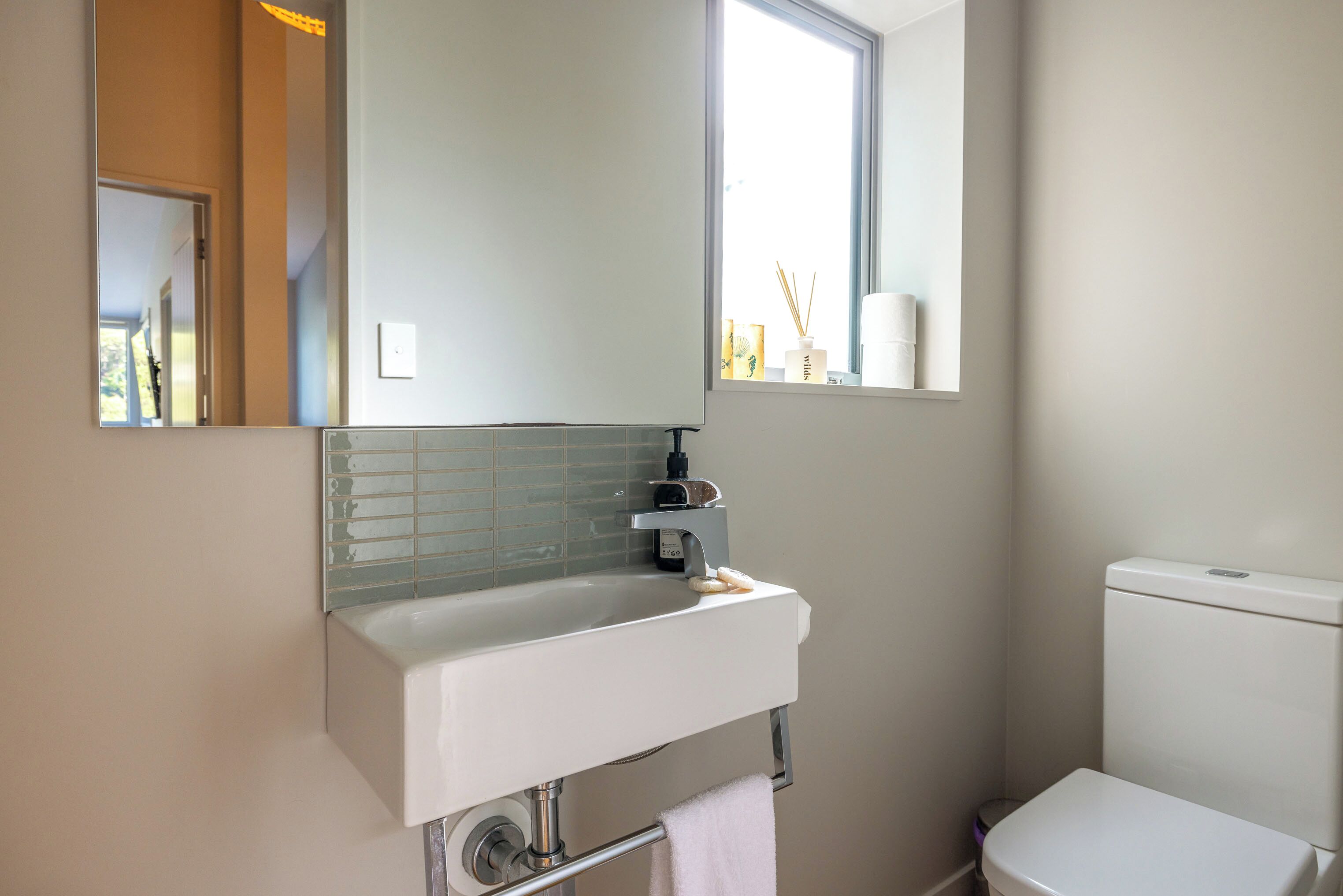 A bathroom with a white sink, a mirror, a window, and a toilet.