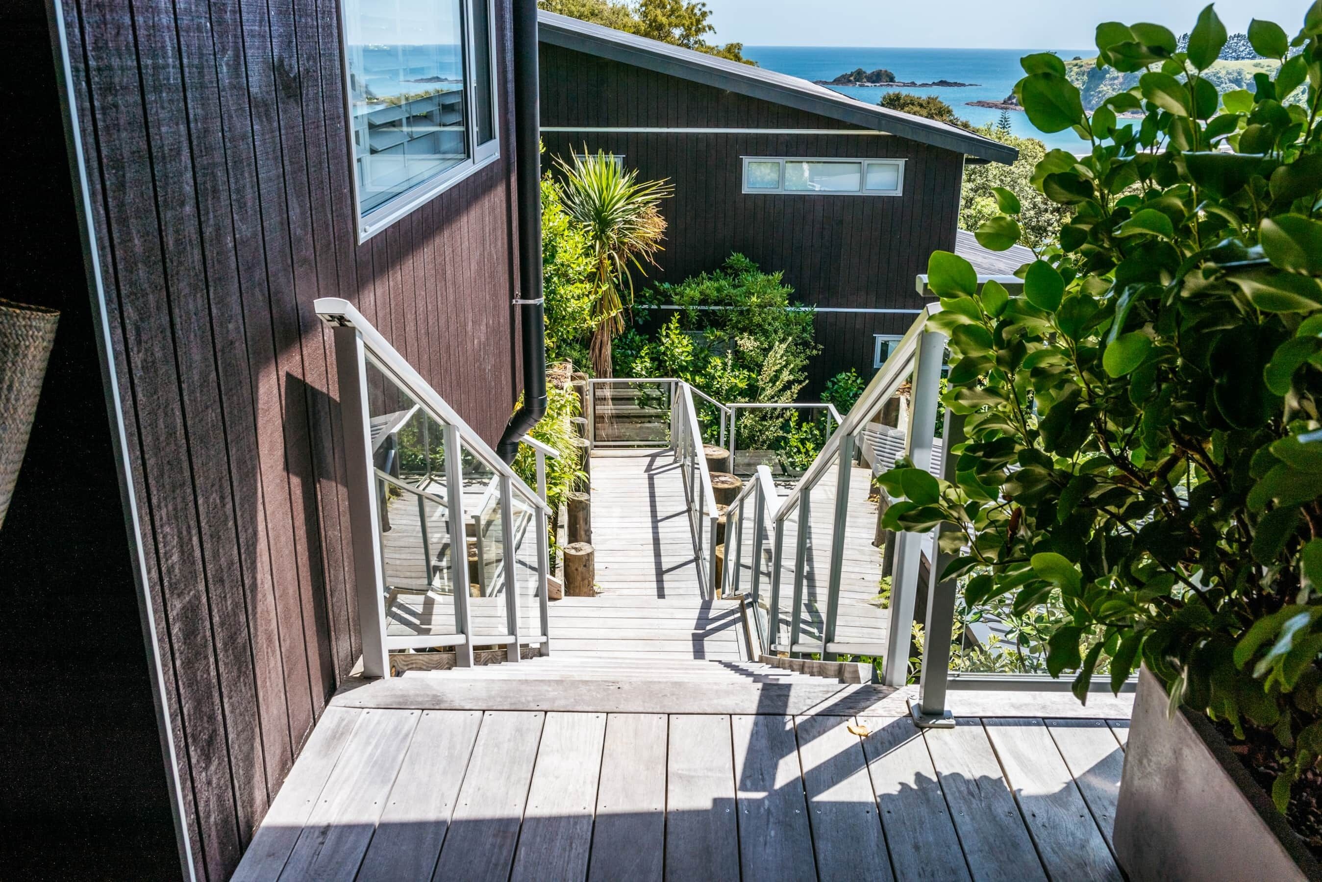 A wooden staircase leading to a modern house with a view of the ocean.