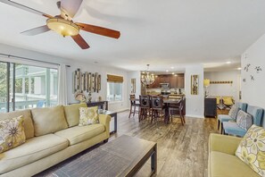 A spacious living room with a large sofa, a coffee table, and a dining area with chairs and a chandelier.