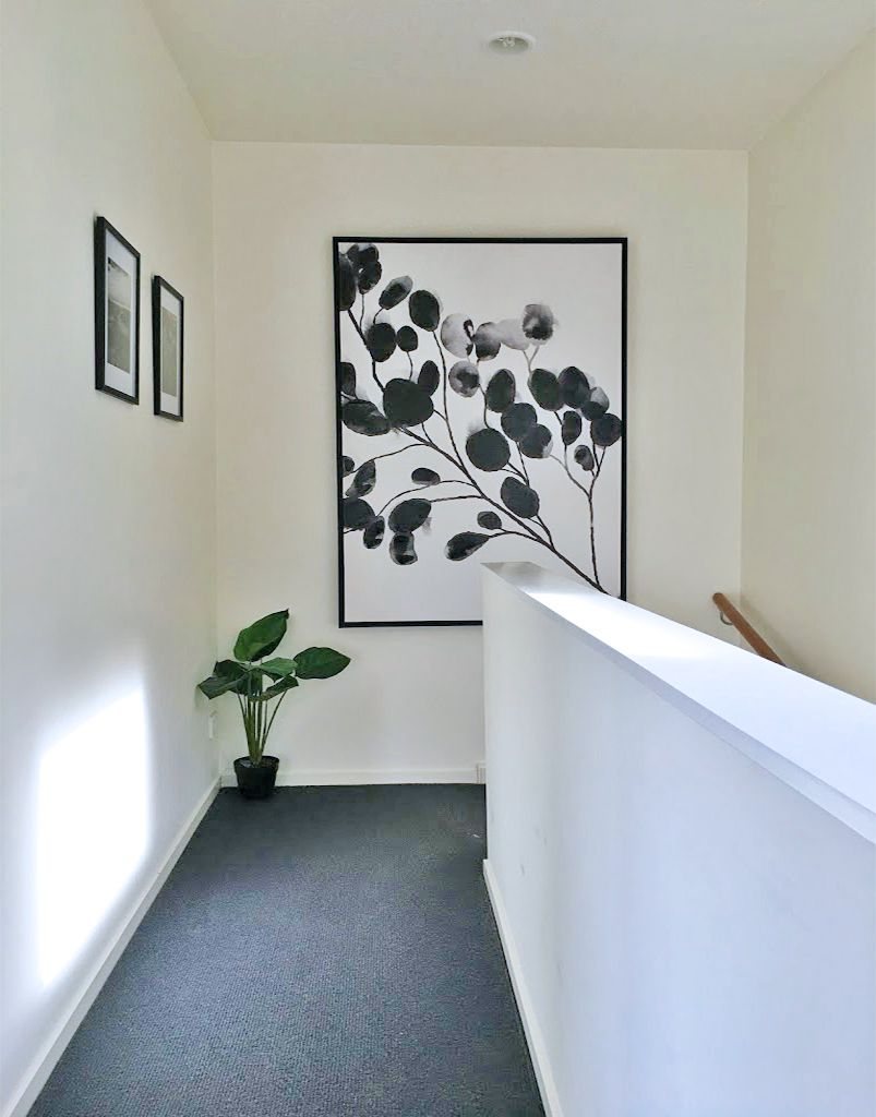 A hallway with a framed artwork on the wall, a potted plant, and a white reception desk.