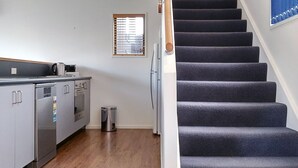 Una cocina moderna con electrodomésticos de acero inoxidable, piso de madera y una escalera con alfombra oscura que lleva a un segundo piso.