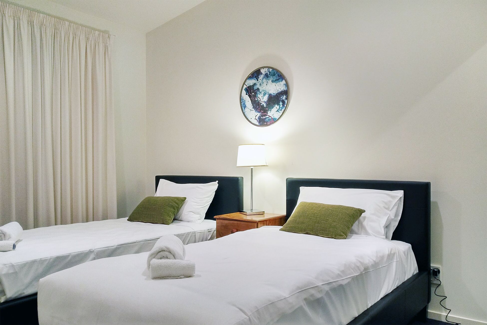 Une chambre d’hôtel avec deux lits, une table de chevet, une lampe et un tableau au mur.