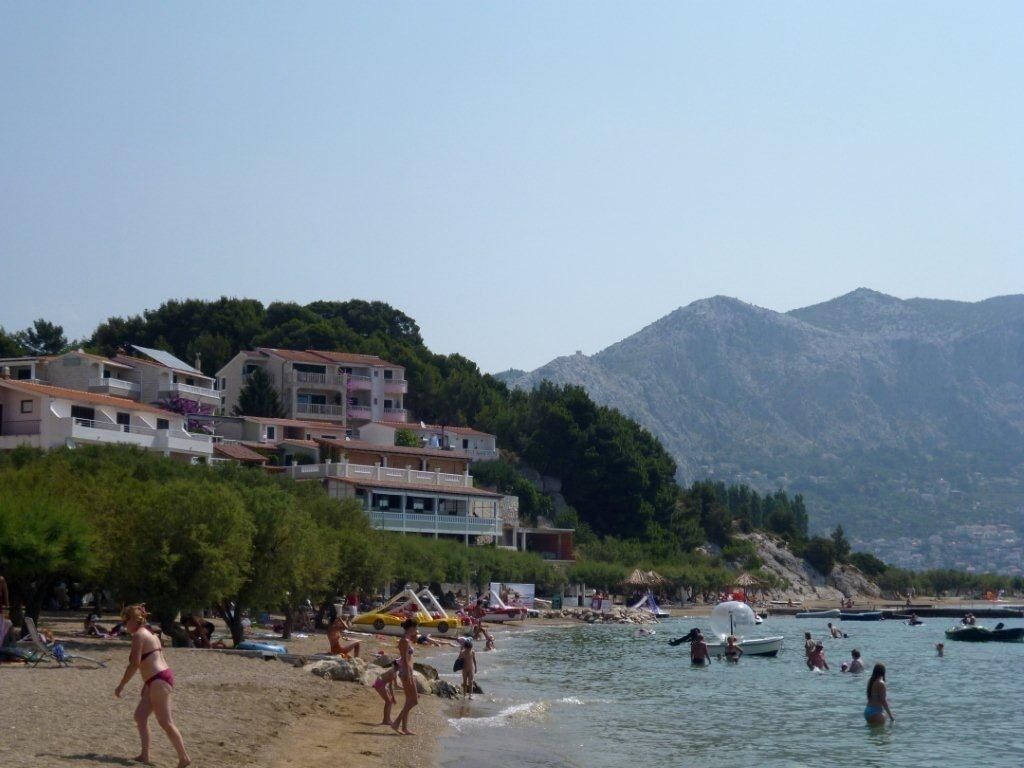 A beach with people, boats, and buildings in the background.