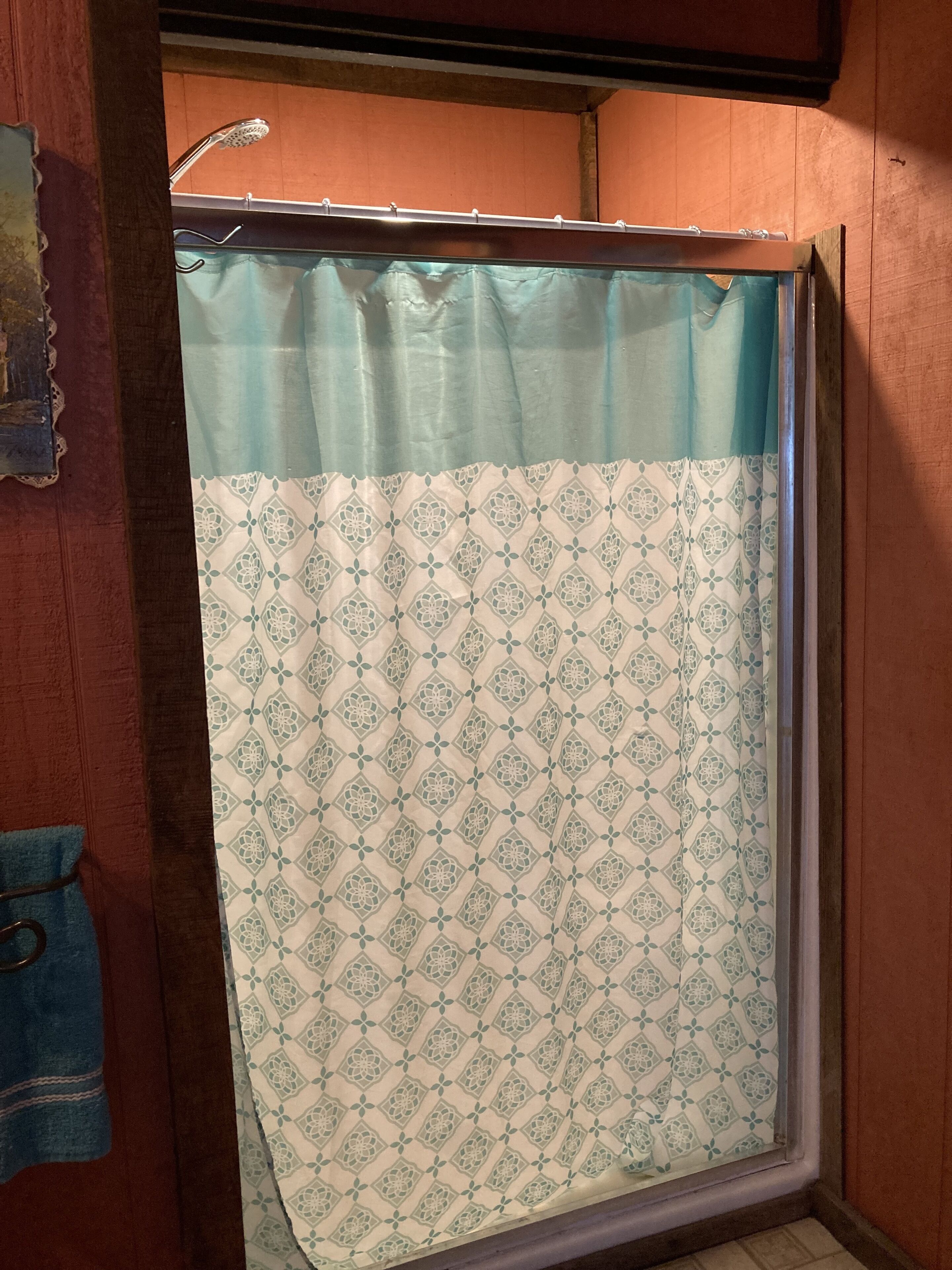 Une salle de bain avec un rideau de douche à motifs, des murs en bois et un porte-serviettes visible.