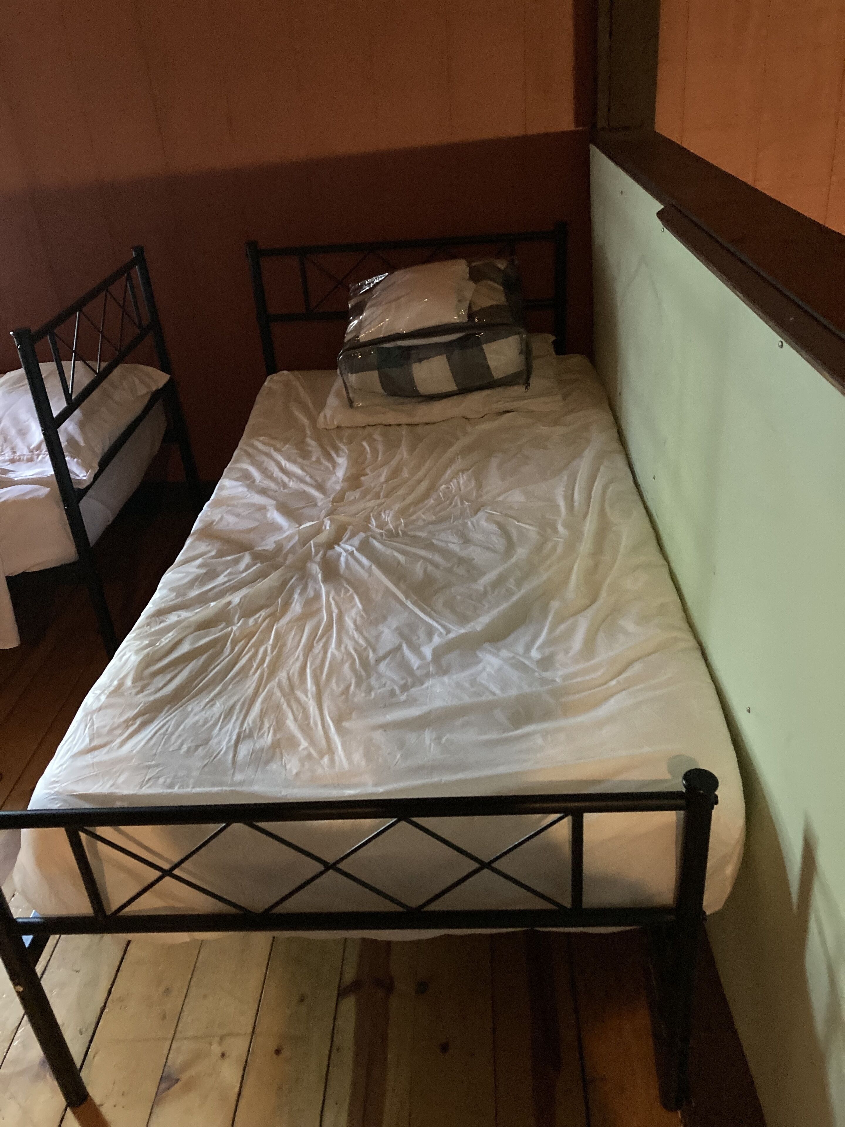 Une petite chambre avec un lit simple, un cadre en métal, un plancher en bois et un mur blanc uni.