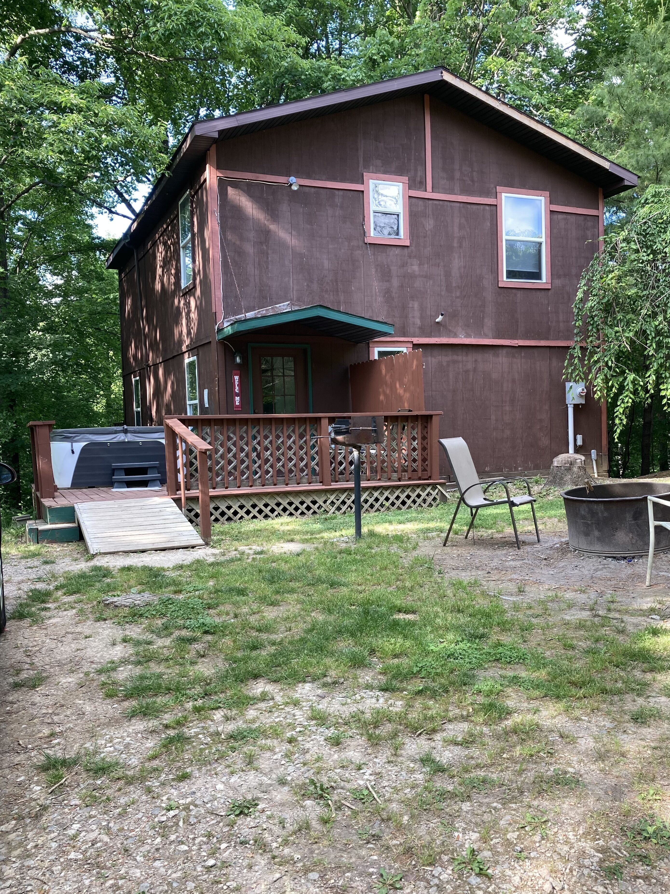 Ein zweistöckiges Holzhaus mit einer Terrasse, einem Grill und einer großen Metalldusche.