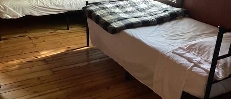 A dormitory room with two single beds, wooden flooring, and a window with curtains.