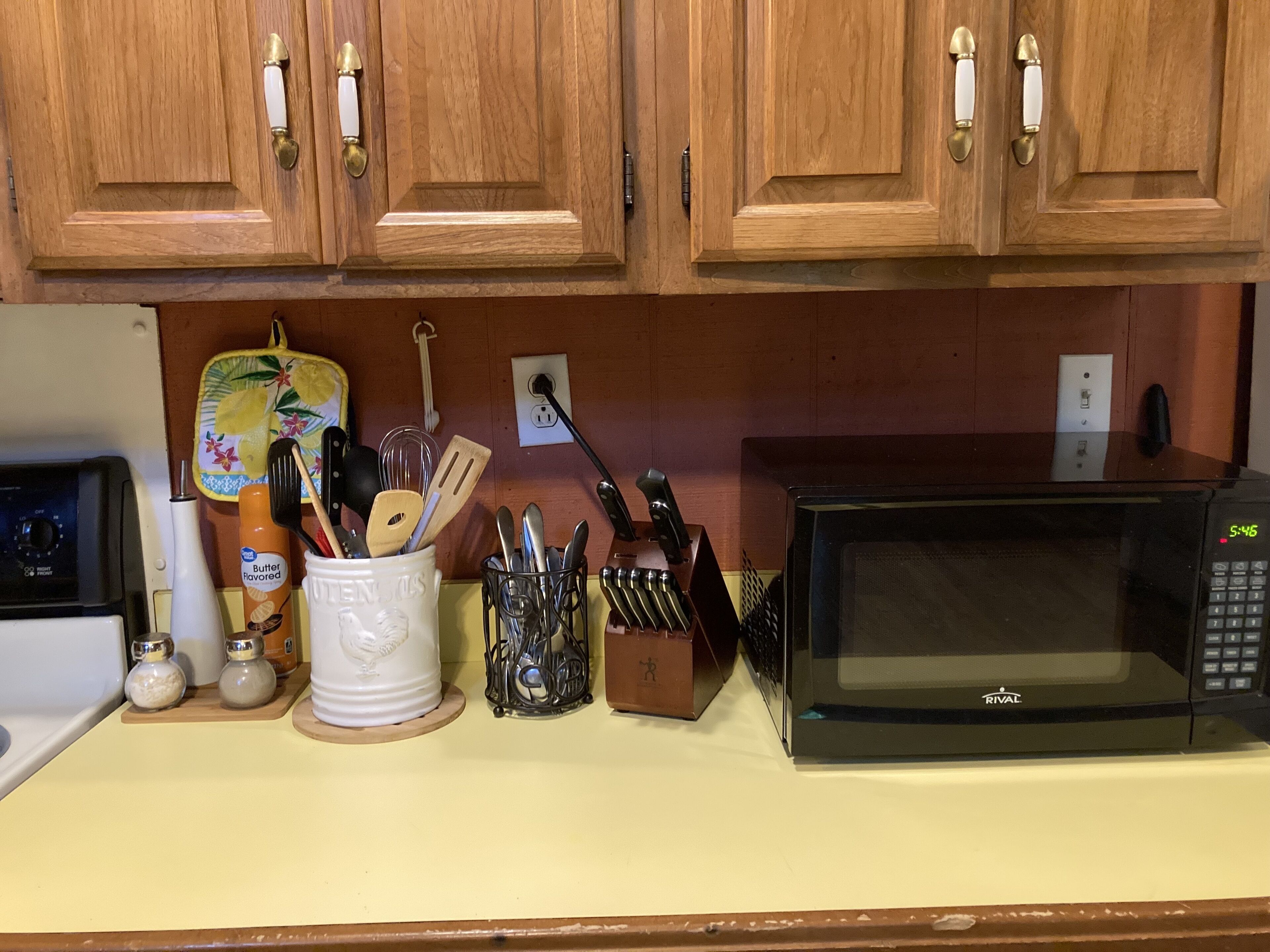 A kitchen with wooden cabinets, a microwave, a toaster, and various kitchen utensils.