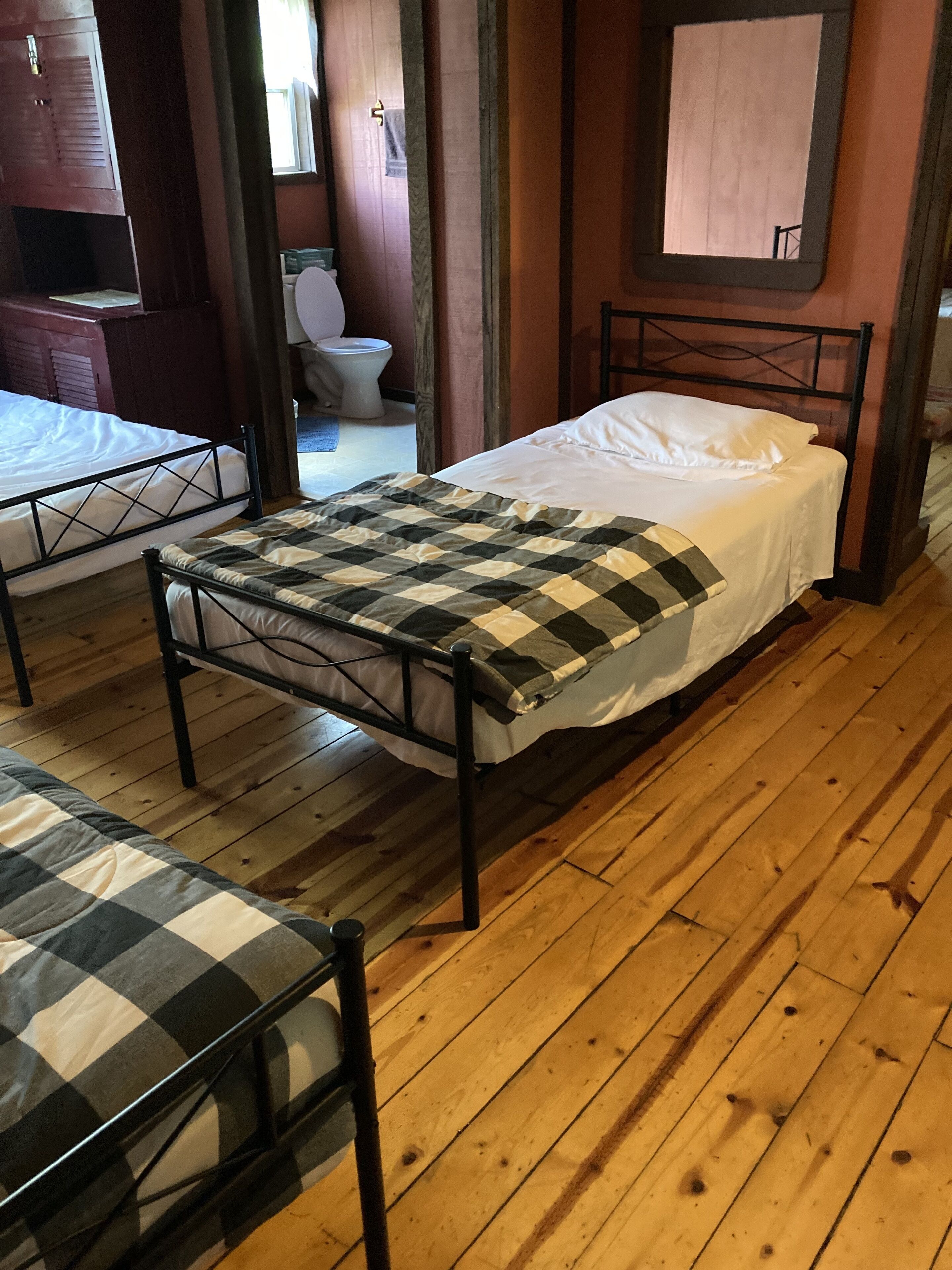 A room with a bed, a bench, a wooden floor, a window, and a door.