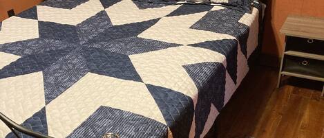 A bed with a star-patterned quilt, a wooden floor, a small nightstand with a lamp, and a rug.