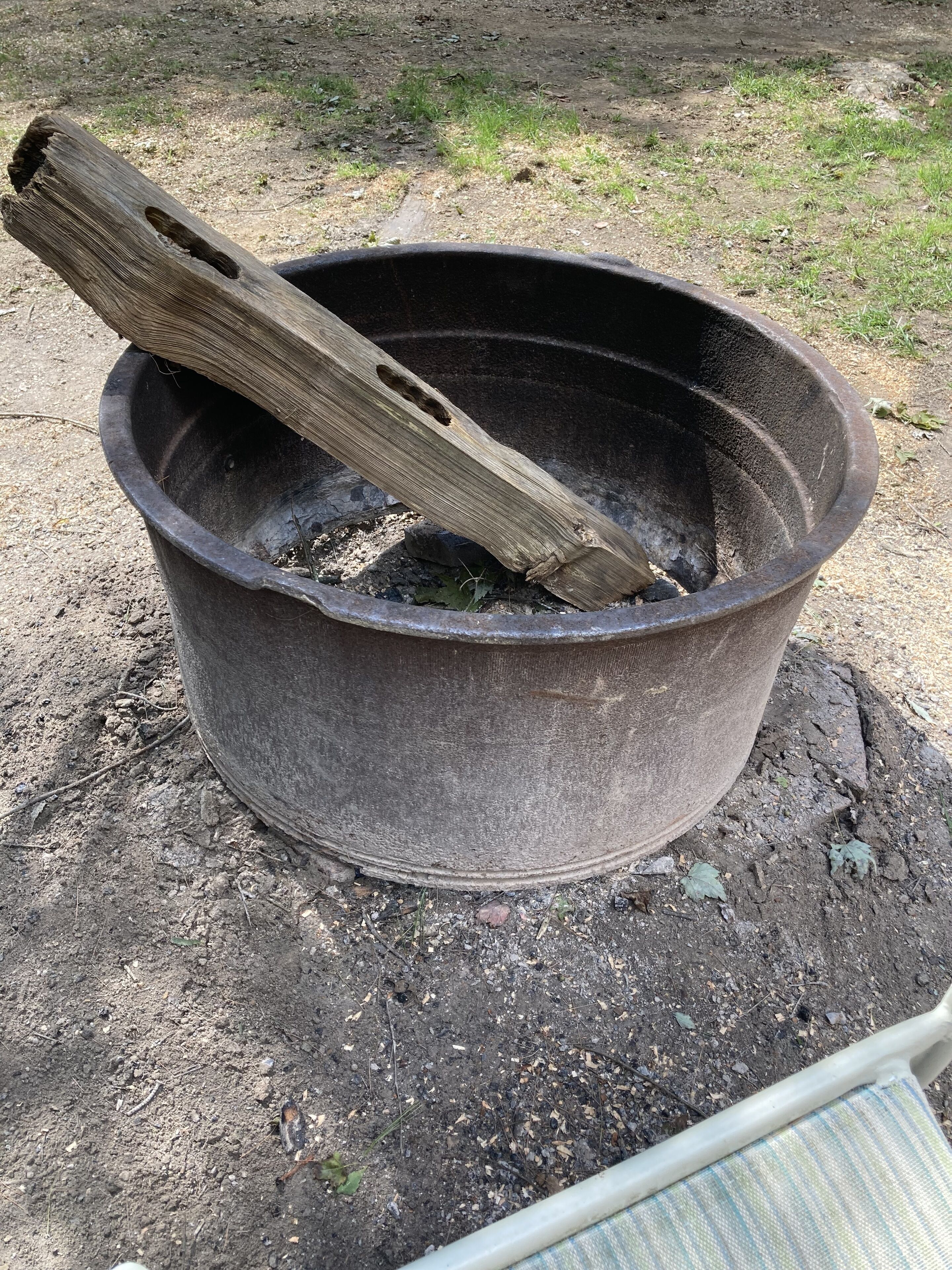 A black pot with a wooden stick inside, placed on a dirt surface.