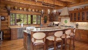 A spacious kitchen with wooden cabinets, a large island with bar stools, and a view of the outdoors through the windows. - HILLTOP HIDEAWAY- A Magical Mountain Ski Estate with Game Room, Hot Tub, and Vie (Telluride)