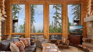 A log cabin interior with a large window, leather furniture, a television, and a stone fireplace. - HILLTOP HIDEAWAY- A Magical Mountain Ski Estate with Game Room, Hot Tub, and Vie (Telluride)