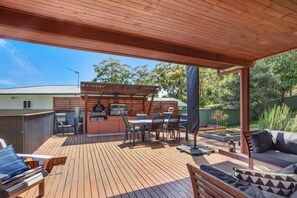 An outdoor patio with a wooden deck, a barbecue area, and a seating arrangement.