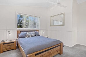 A bedroom with a bed, bedside tables, a ceiling fan, a window with blinds, and a mirror on the wall. - Ocean Beach Pet Friendly near Shoal Bay Beach (Shoal Bay)
