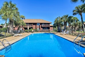 A swimming pool with lounge chairs, surrounded by palm trees and a building with balconies.