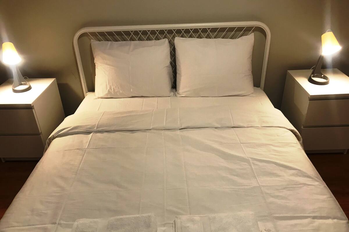 A neatly made bed with white bedding, two bedside lamps, and a metal headboard.