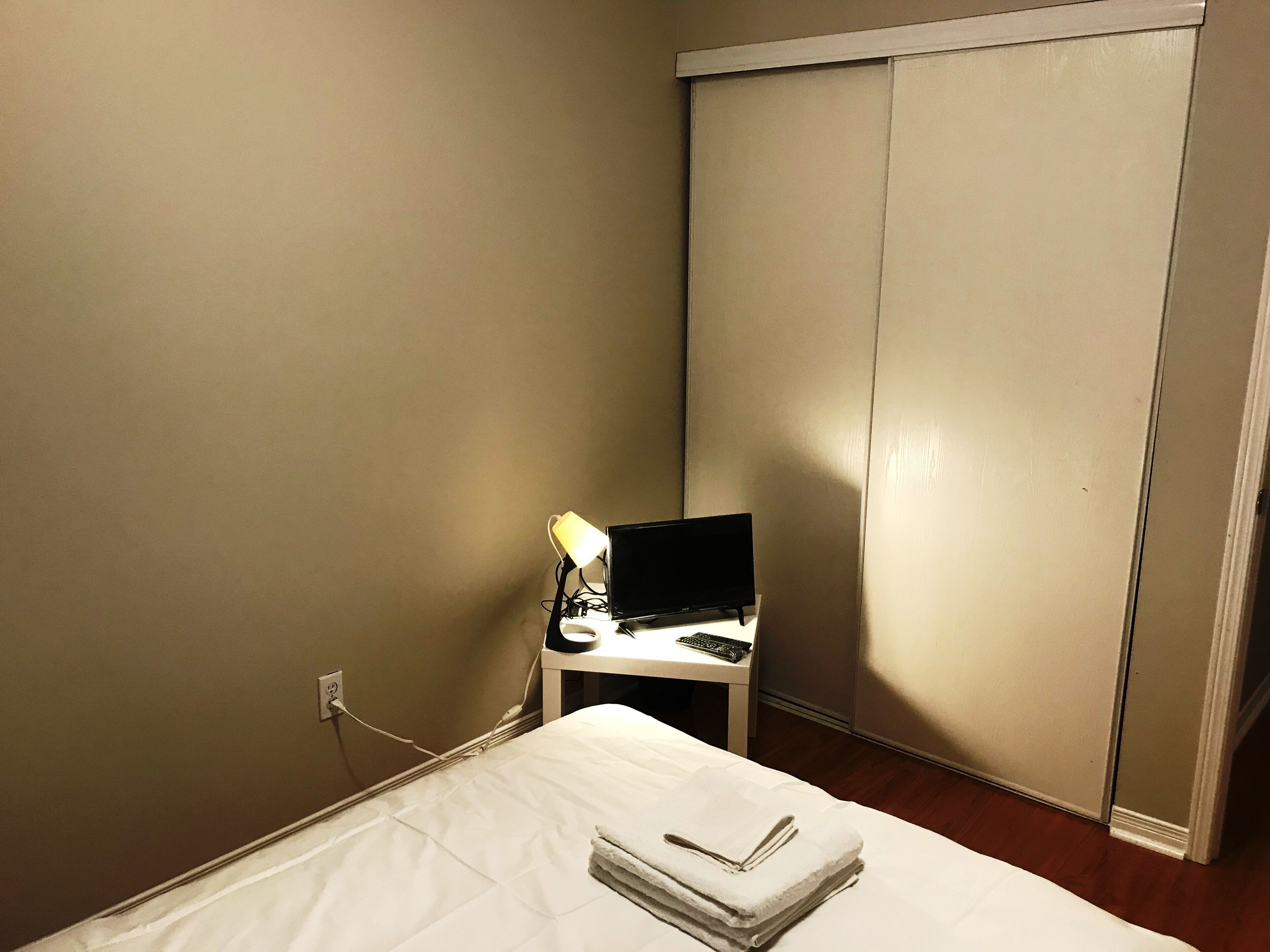 Un dormitorio pequeño con una cama, un escritorio con una computadora y una lámpara, además de un armario.