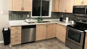 A kitchen with wooden cabinets, a dishwasher, a stove, and a microwave. - Guardian Cottage (Mississauga)