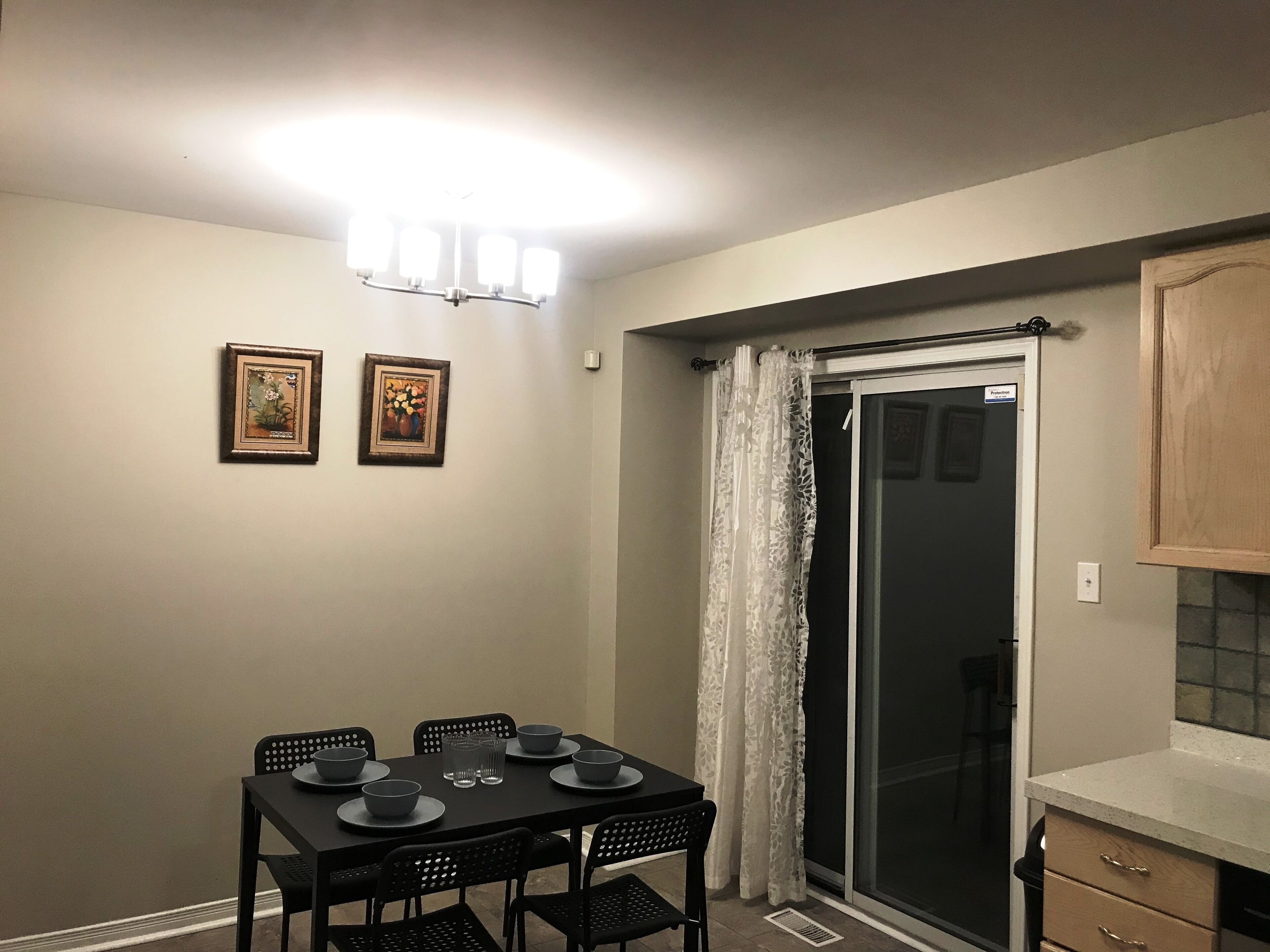 A dining area with a table set for four, chairs, and two framed pictures on the wall.