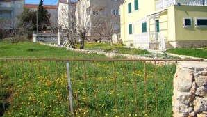 A residential area with a yellow building, stone wall, and a grassy field with yellow flowers. - Apartment in Ždrelac with Seaview, Balcony, Air condition, WIFI (4561-1) (Ždrelac)