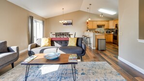 A modern living room with a sofa, coffee table, and a dining area with a chandelier. - Accommodating Anchorage Abode < 1 Mi to Jewel Lake (Anchorage)