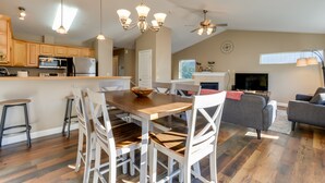 A modern kitchen with wooden cabinets, a dining area with a wooden table and white chairs, a grey sofa, and a ceiling fan. - Accommodating Anchorage Abode < 1 Mi to Jewel Lake (Anchorage)