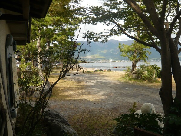 Vista de un lago con montañas al fondo, una zona pavimentada en primer plano y árboles.