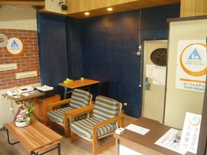 A youth hostel reception area with a wooden desk, two striped chairs, a small table, and a blue wall. - Youth Hostel WANIHIMA~Lakeside BIWA (Otsu)