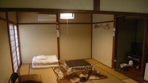 A traditional Japanese room with tatami flooring, a futon bed, a low table, a chair, and a television in a corner. - Youth Hostel WANIHIMA~Lakeside BIWA (Otsu)