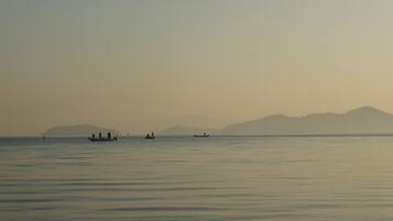 A calm body of water with several boats and distant mountains under a hazy sky.