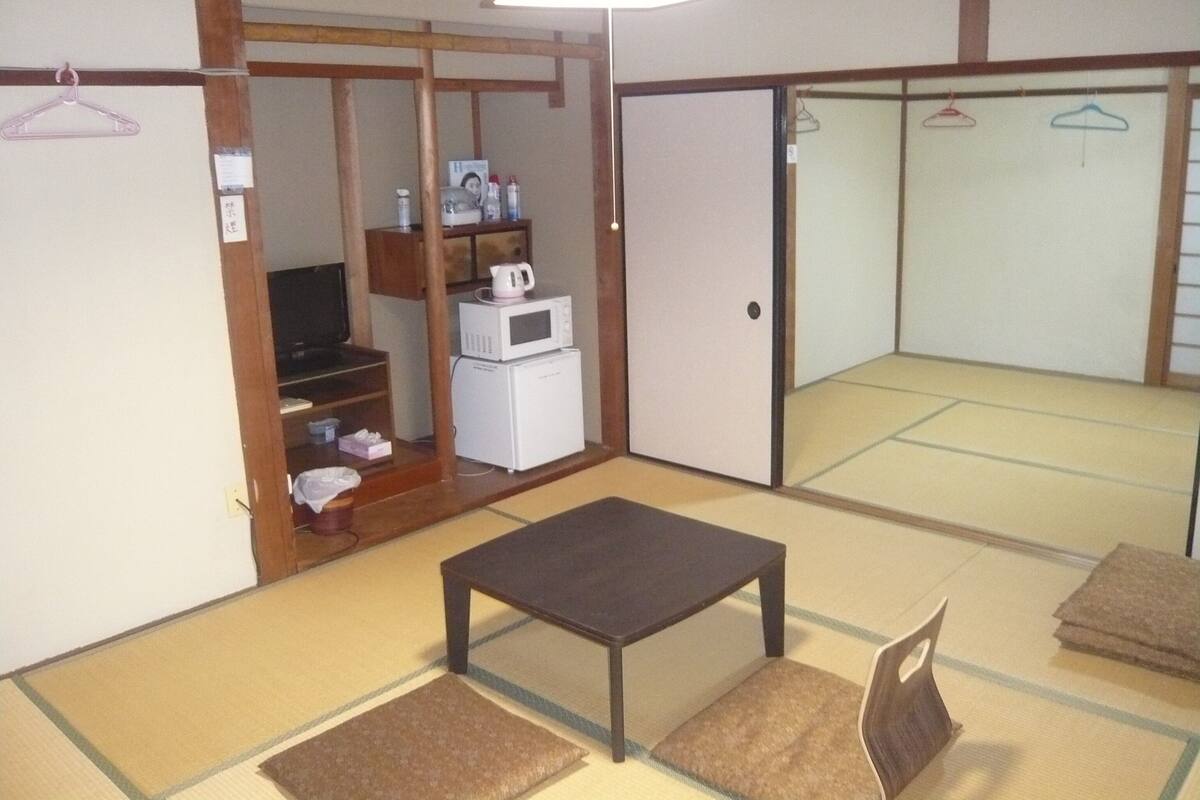Une pièce de style japonais traditionnel, avec un sol recouvert de tatamis, une table basse, un téléviseur et une armoire à portes coulissantes.