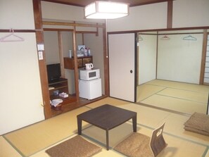 A traditional Japanese room with tatami flooring, a low table, a TV, and a wardrobe with sliding doors. - Youth Hostel WANIHIMA~Lakeside BIWA (Otsu)