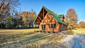 A wooden cabin with a green roof, surrounded by trees and a gravel path.